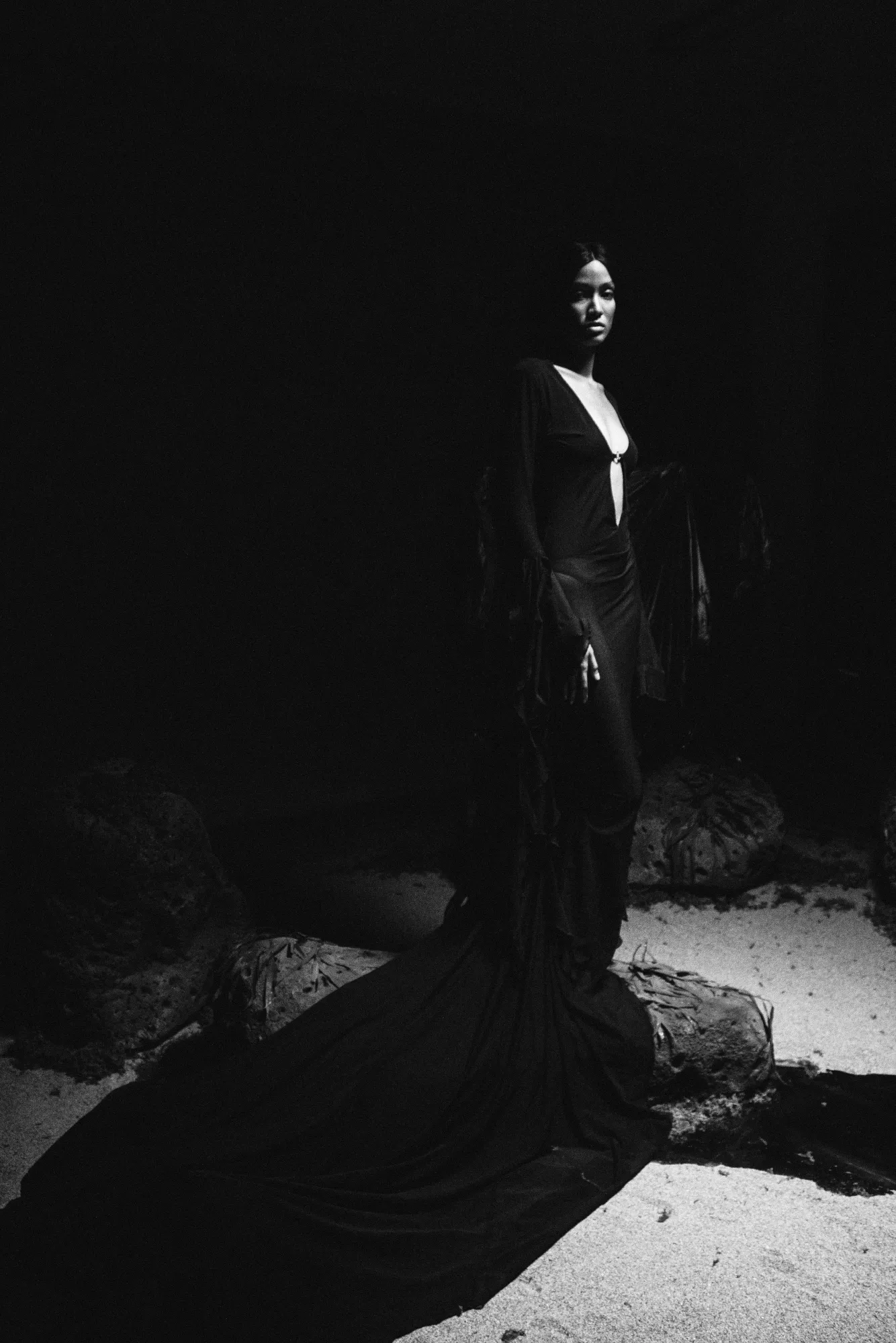 Figura vestida de negro, de pie sobre la arena en una penumbra cálida.